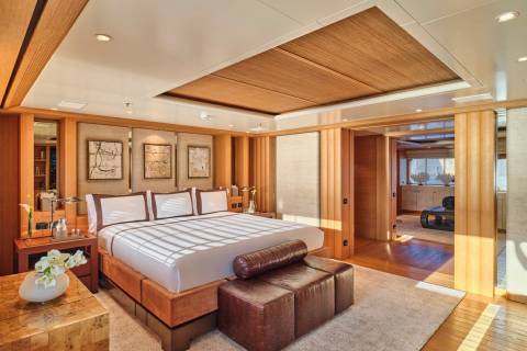 Luxurious yacht master suite features a king-sized bed, warm wood accents, and an adjacent sitting area with ocean views.