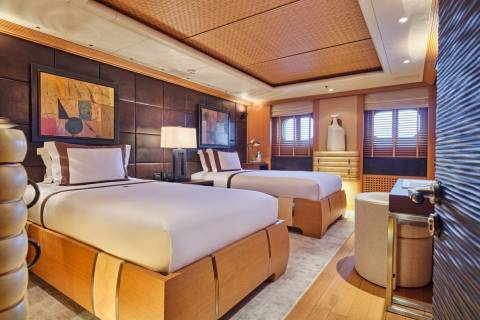 Luxurious twin beds with rich wood accents and abstract art create a serene and stylish cabin aboard this opulent yacht.