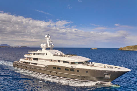 A luxurious superyacht cruises through the deep blue sea under a cloudy sky near a rocky island.