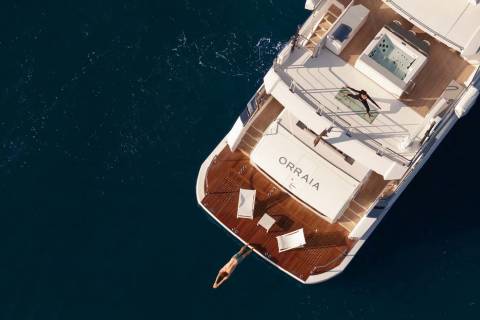 A person dives into the deep blue sea from the luxurious yacht Orraia, while another practices yoga on deck.