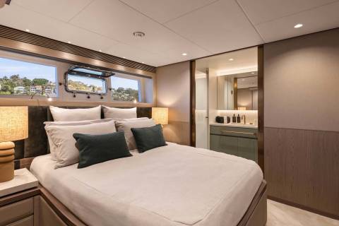 Luxurious yacht cabin offers a serene retreat with a plush bed, elegant lighting, and a glimpse of a scenic coastal view.