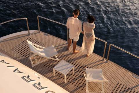 A couple gazes out at the ocean from the deck of a luxurious yacht, enjoying a serene moment at sea.