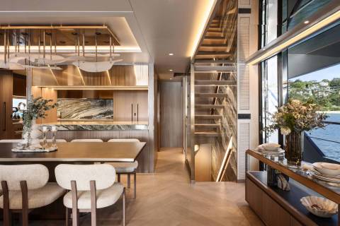 A modern dining area with a marble-accented kitchen and a striking staircase overlooks a serene waterfront vista.