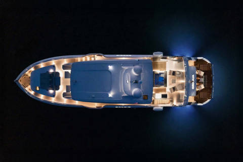 This aerial view captures a luxurious yacht illuminated at night, its interior lights casting a warm glow on the dark water.