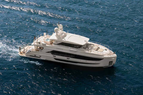 A luxurious white yacht glides through the sparkling blue ocean, leaving a foamy wake.