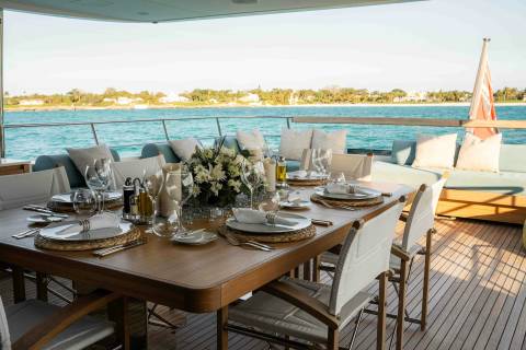 An elegant outdoor dining setting awaits guests on a yacht deck overlooking a serene turquoise sea.