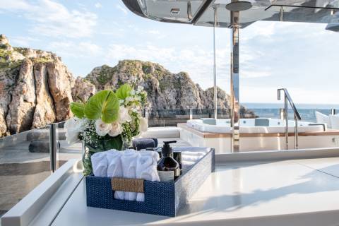 A bouquet of white roses and green anthuriums adorns a yacht deck overlooking rocky cliffs and the azure sea.
