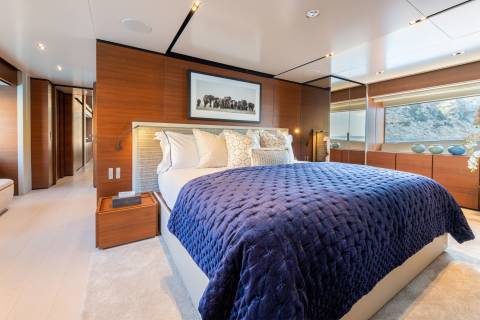 Luxurious dark blue bedding adorns a spacious bedroom with wood-paneled walls and a scenic ocean view.