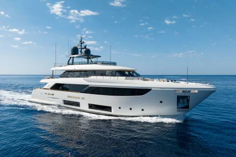 A sleek white yacht glides through the deep blue ocean under a bright, cloud-dappled sky.