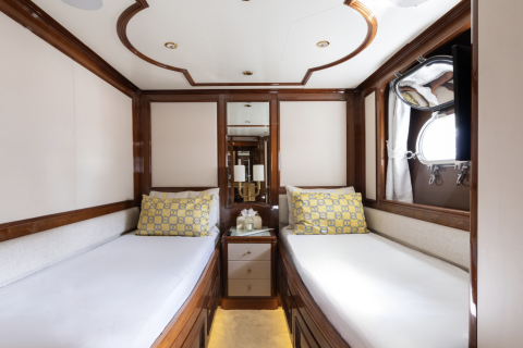 Luxurious twin beds with yellow patterned pillows are neatly made in this elegant yacht cabin.