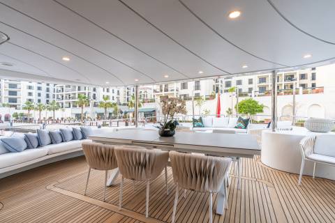 Luxurious outdoor seating on a yacht deck offers a serene dining experience with a backdrop of modern architecture and palm trees.