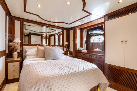 Luxurious yacht cabin features a plush bed, elegant wood paneling, and porthole windows offering a glimpse of the sea.