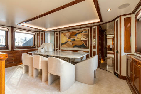 Luxurious dining on this yacht features a marble table, plush seating, and a striking abstract artwork.