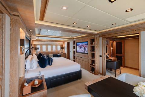 Luxurious yacht stateroom features a king-size bed, large television, and elegant wood finishes.