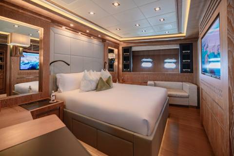 Luxurious yacht accommodations feature a spacious master suite with a king-sized bed, elegant wood finishes, and a large entertainment system.
