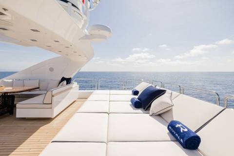 Luxurious white cushions and plush navy pillows invite relaxation on the sun-drenched deck of a yacht overlooking the tranquil blue sea.
