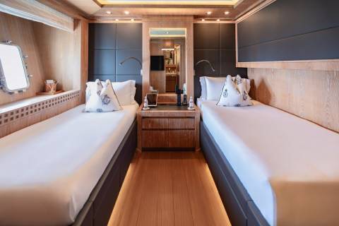 Twin beds are neatly made with nautical-themed pillows in this luxurious yacht cabin.