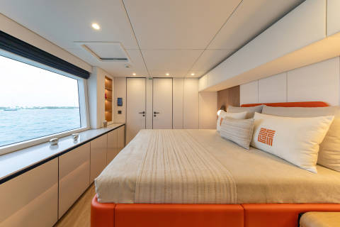 A cozy and modern bedroom with a large window overlooking a body of water, featuring a comfortable bed, built-in storage, and a minimalist design.