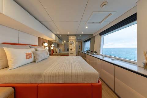 A spacious and modern hotel room with a large bed, wooden furniture, and a panoramic window overlooking the ocean.