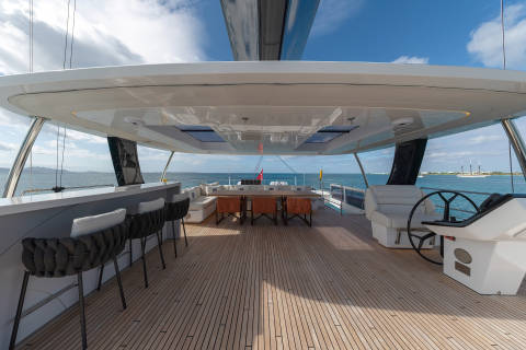 A modern, luxurious yacht deck with a covered seating area, wooden flooring, and a scenic view of the ocean and sky in the background.