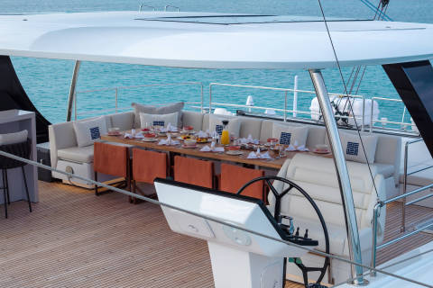 A luxurious yacht with a well-appointed outdoor dining area overlooking a serene, turquoise-colored sea.