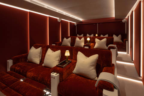 A cozy and luxurious home theater with plush burgundy seating, decorative pillows, and subtle lighting, creating an inviting and comfortable atmosphere.