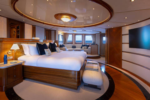 A luxurious and spacious bedroom with a large circular bed, wooden furnishings, and a panoramic view of the surrounding landscape through the large windows.