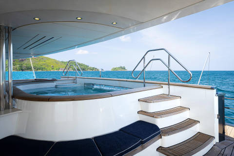 A luxurious yacht with a built-in swimming pool on the deck, surrounded by a picturesque seascape with mountains in the background.