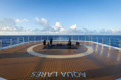 A wooden deck with a circular pattern on a cruise ship, overlooking the vast expanse of the open ocean and a cloudy sky.
