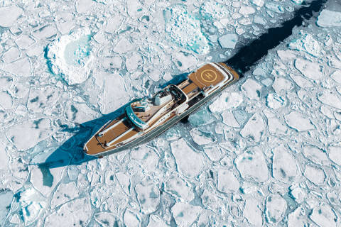 A small wooden boat navigates through the frozen, icy waters, surrounded by a vast expanse of ice and snow.
