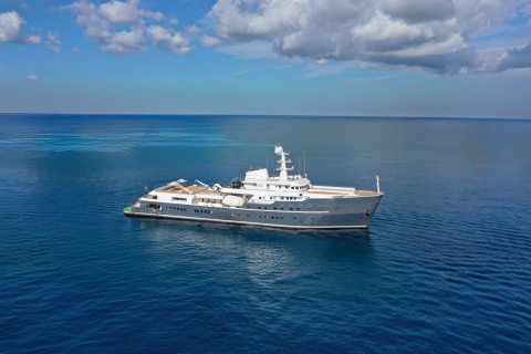 A large, luxurious yacht is floating on the serene, turquoise waters of the ocean, surrounded by a clear blue sky dotted with fluffy white clouds.