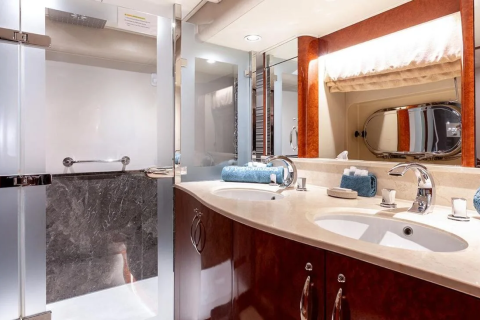 A luxurious yacht bathroom features a modern double vanity in the foreground and a glass-enclosed shower in the background.