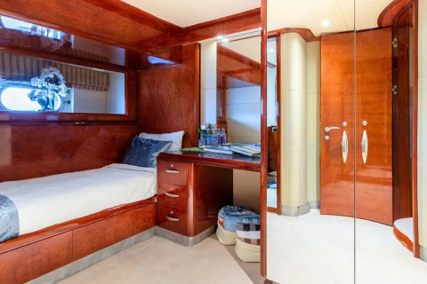 A neatly made single bed with blue accents sits in the foreground, while the background reveals a polished wooden desk and a mirrored closet door.