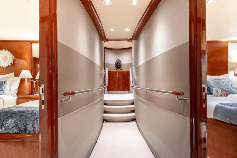 A well-lit hallway with two bedrooms visible on either side leads to a staircase at the end of the yacht.