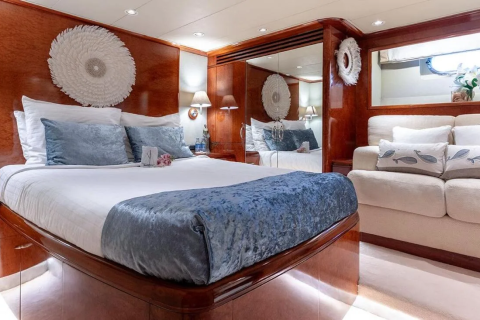A luxurious yacht bedroom features a large bed with blue accents in the foreground and a plush sofa with whale-themed pillows in the background, all set against rich wood paneling and a mirrored wall.