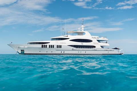 A large white yacht floats on turquoise water under a bright blue sky with scattered clouds.
