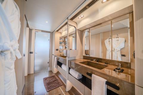 Fluffy white robes hang in the foreground of a luxurious bathroom with dual sinks and large mirrors reflecting more robes in the background.
