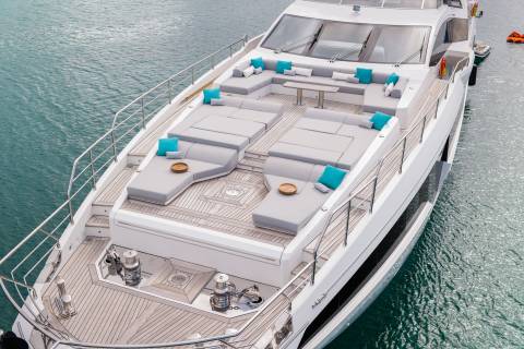 A luxurious white yacht with plush gray seating and bright turquoise cushions is docked in calm, blue water.