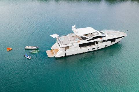 A large white yacht is anchored in calm blue water, with several smaller watercraft floating nearby.