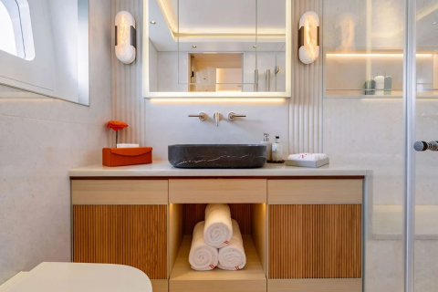 A modern bathroom features a black stone sink and wooden vanity in the foreground, with a large mirror and illuminated wall sconces in the background.