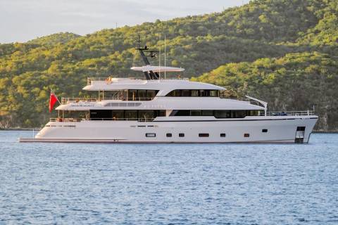 A large white yacht sails on calm blue water in the foreground, with lush green hills rising in the background.