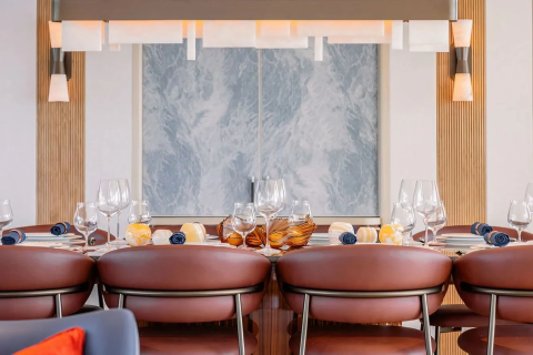 A formal dining table with brown leather chairs in the foreground is set with glassware and place settings, while a marbled wall and modern light fixture adorn the background.