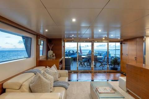 A luxurious yacht interior with a plush white sofa in the foreground and a deck with ocean views in the background.