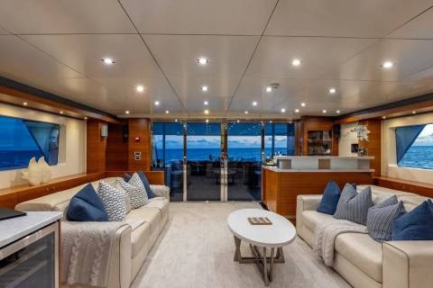 A luxurious yacht interior with plush sofas and a coffee table in the foreground, and a stunning ocean view through large windows in the background.