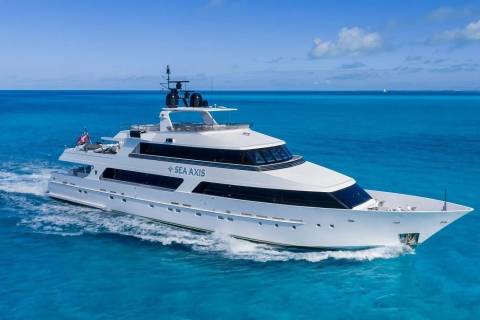 A large white yacht cruises through turquoise waters under a bright blue sky with scattered clouds.