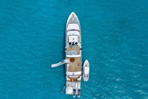 A large white yacht with a slide and a smaller boat are anchored in crystal clear turquoise water.