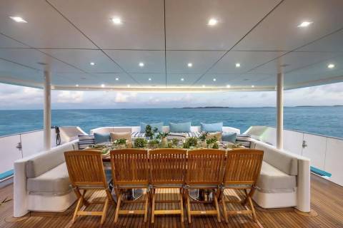 A beautifully set dining table with chairs on a yacht's deck overlooks a calm ocean under a cloudy sky.