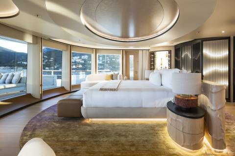 A luxurious bedroom with a large bed in the foreground and a scenic view of a bay with boats and hills in the background.