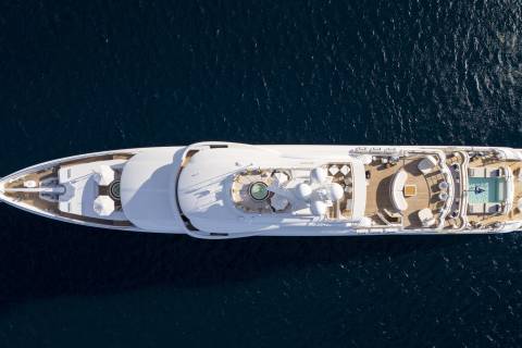 A luxurious white yacht with multiple decks and a pool sails on the deep blue ocean.