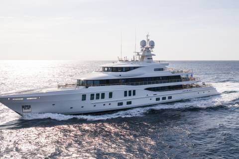 A large white yacht cruises through calm, sun-dappled ocean waters under a bright sky.